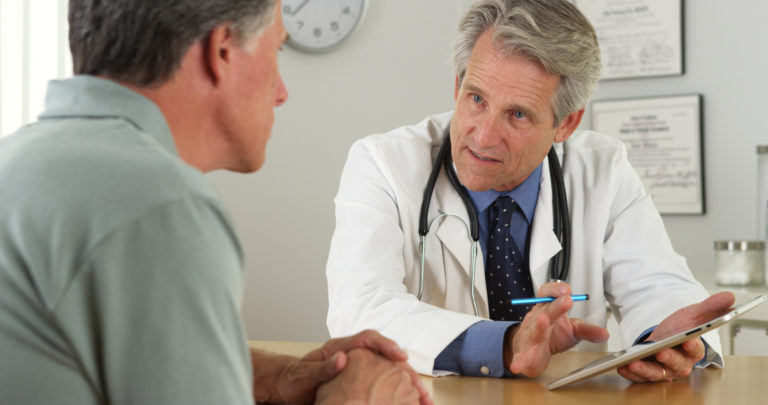 Senior doctor talking with patient and tablet in office
